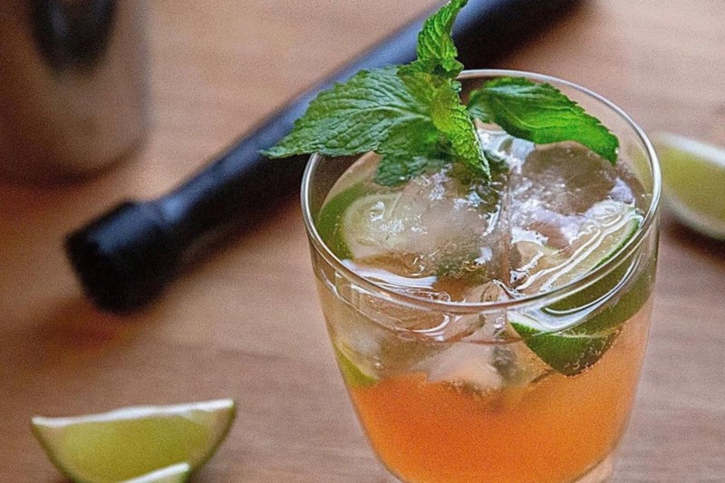 A close-up of a glass of Nectarine Mojito with mint leaves beside slices of lime.