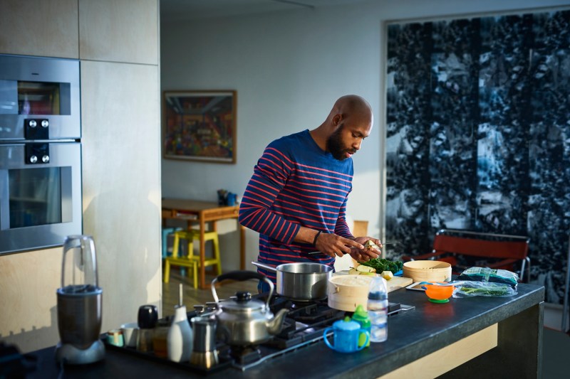 A man in a red and blue striped long sleeved shirt prepares healthy food in his kitchen.
