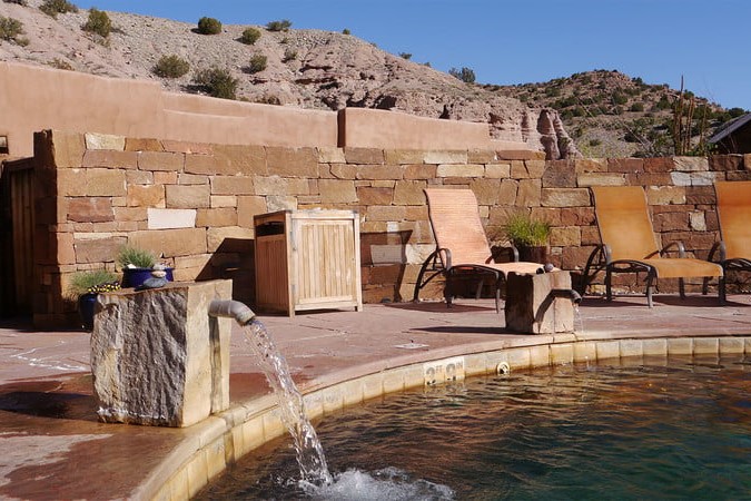 A mineral springs area with some brown chairs surrounding it. There are dry hills and green bushes in the background.