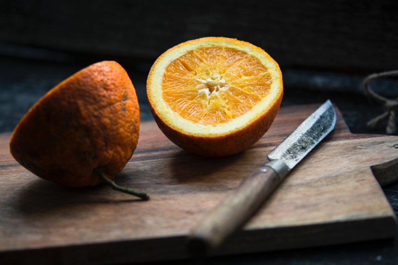 Orange sliced in half by knife on cutting board.