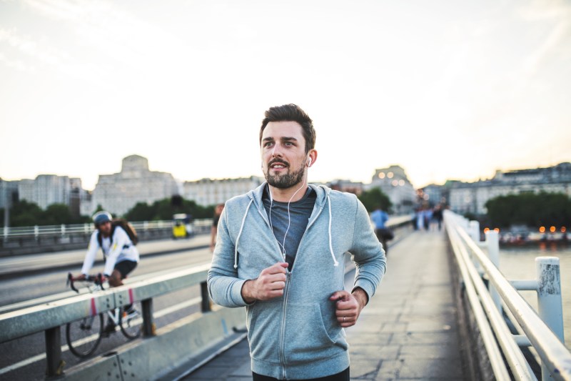 A man in jacket and earphones jogging on the street.