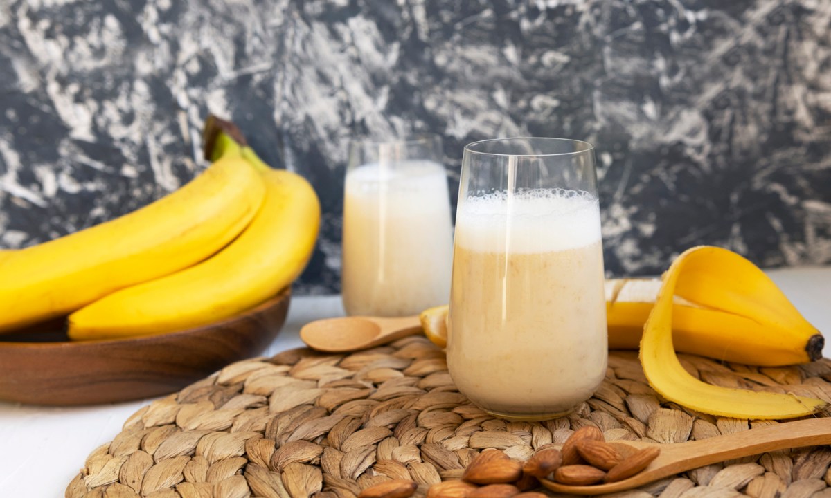 A banana shake with bananas, nuts, wooden spoons, coaster, and a glass of milk.