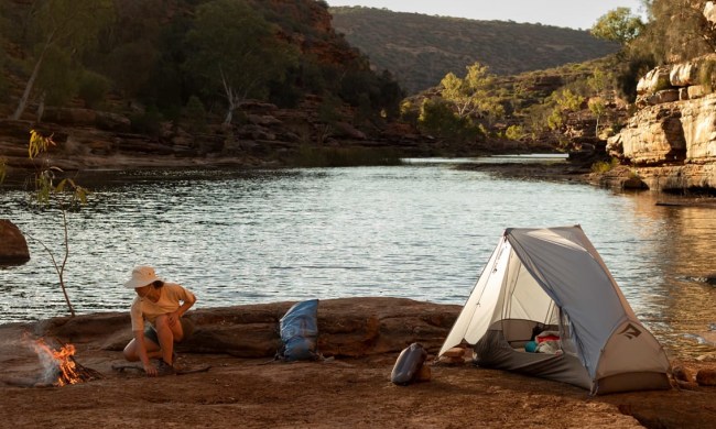 Person camping on a river using a one person tent.
