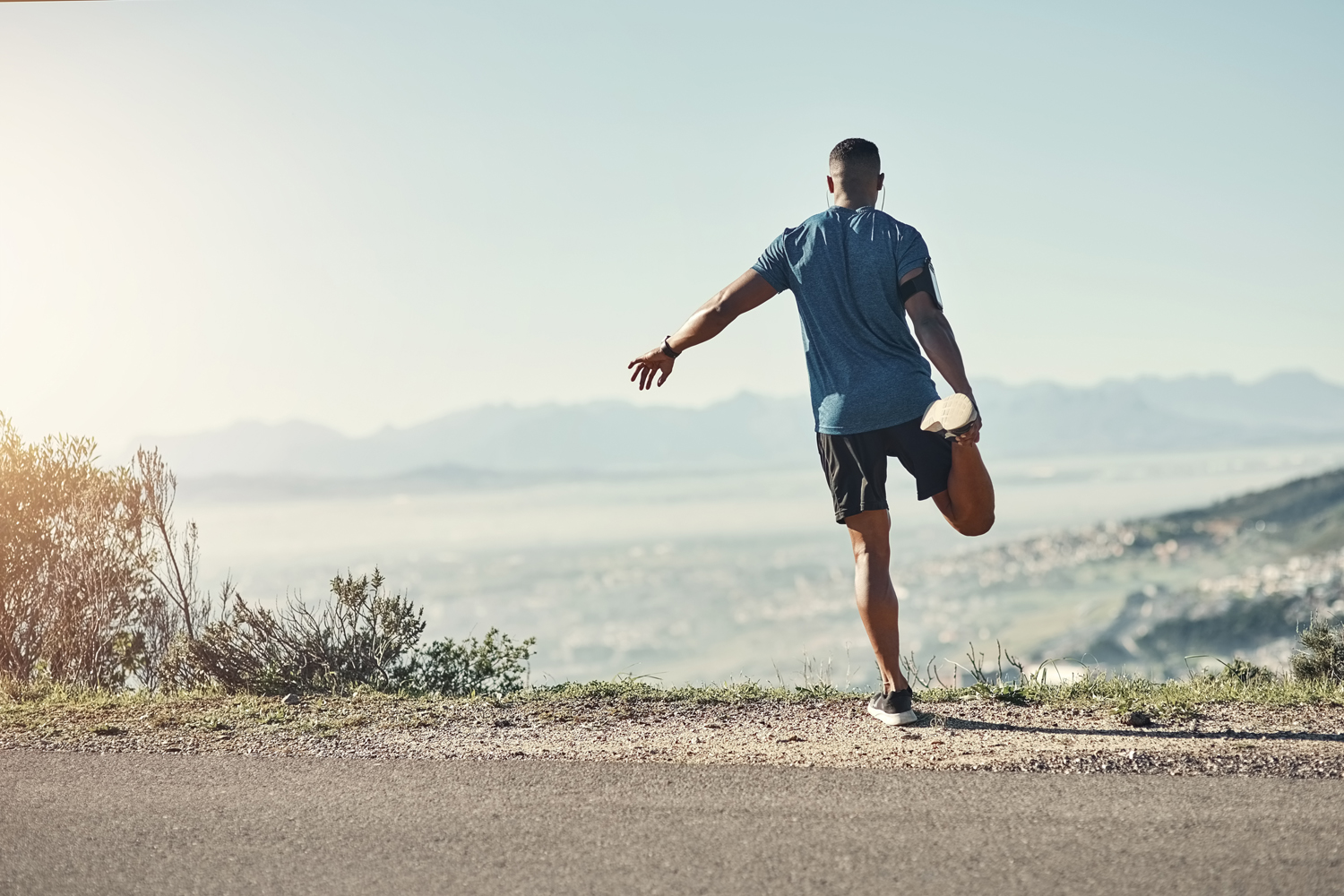 A man balancing on one leg on a road with a view of the mountain.