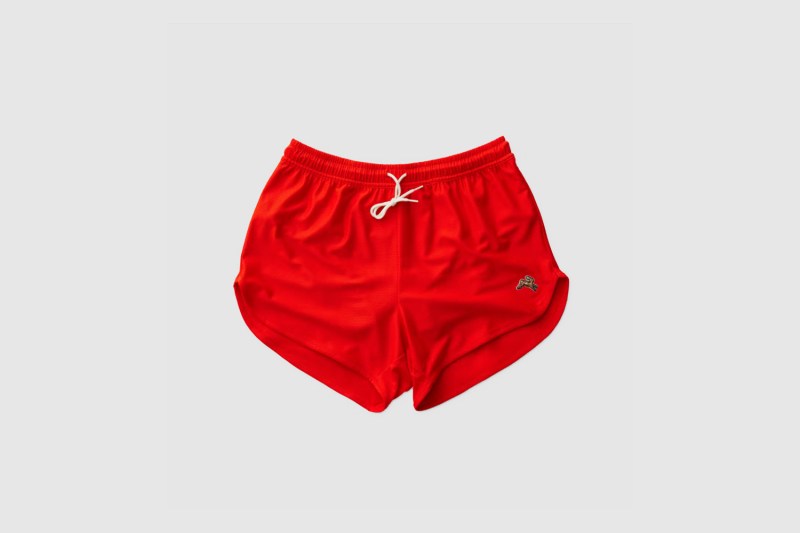 A pair of red Tracksmith Van Cortlandt Shorts on gray background.