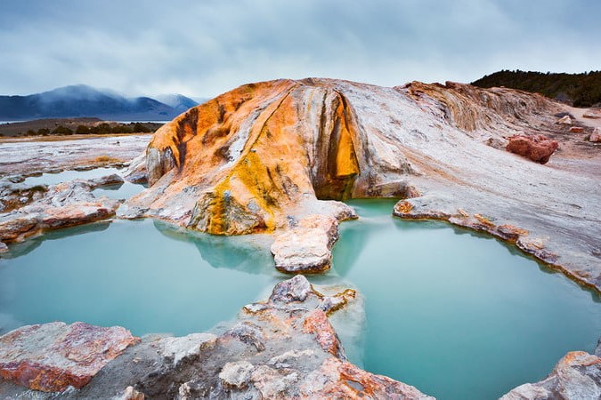 A blue hot springs pool, surrounded by rocks that are white, red, and orange.