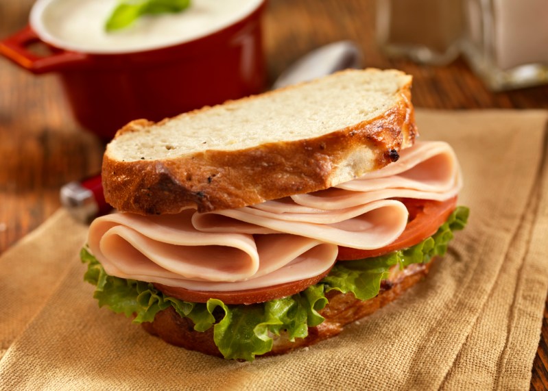 Un sándwich de pavo con verduras en tela marrón y un tazón de sopa de champiñones en el fondo.