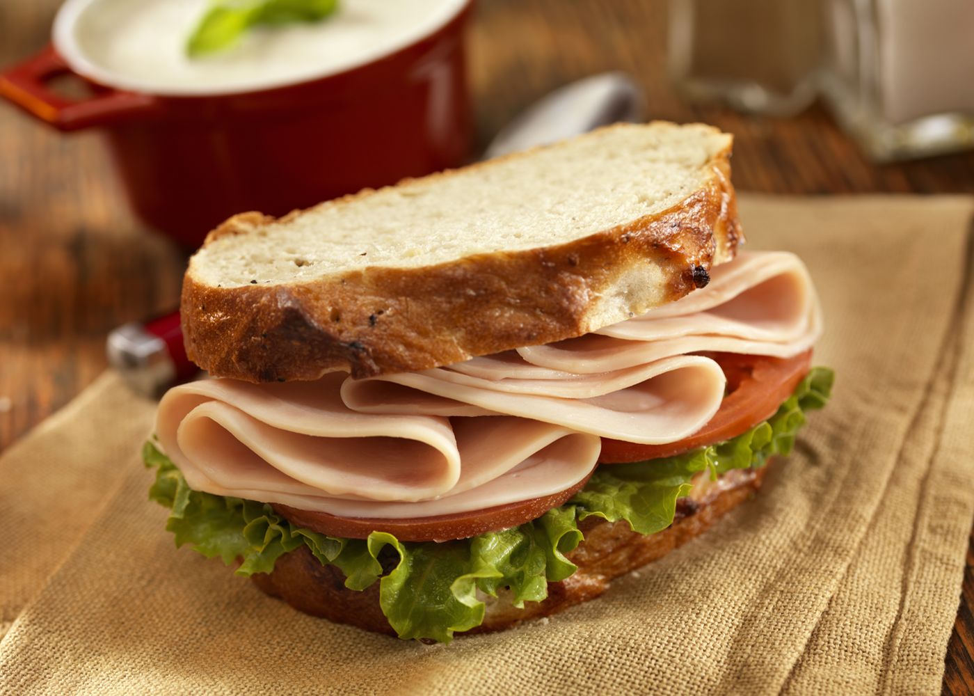 Un sándwich de pavo con verduras en tela marrón y un tazón de sopa de champiñones en el fondo.