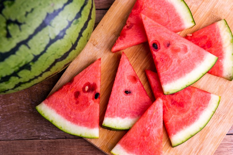 Slices of watermelon on wooden cutting board beside a whole watermelon.