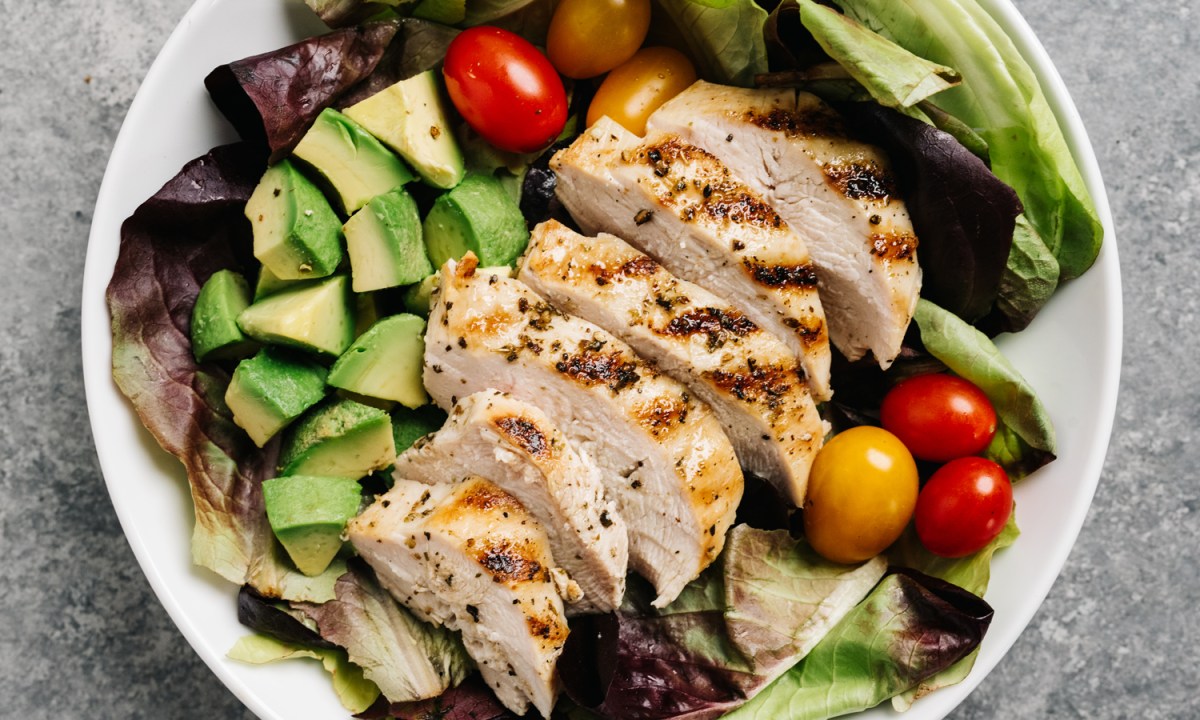 An overhead shot of a bowl of grilled chicken salad on a table