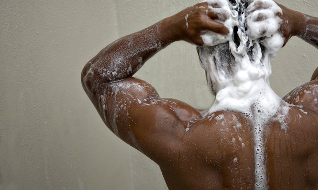 A man lathering shampoo on his head in the shower, suds building up on the back of his neck.