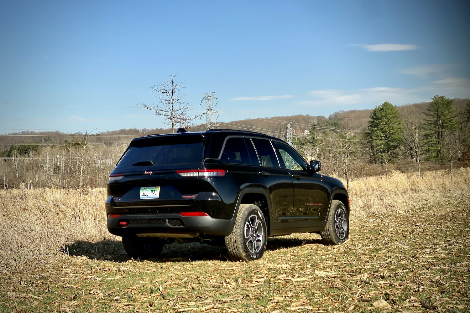 Rear view of the 2022 Jeep Grand Cherokee Trailhawk in a grassy field in front of bushes.
