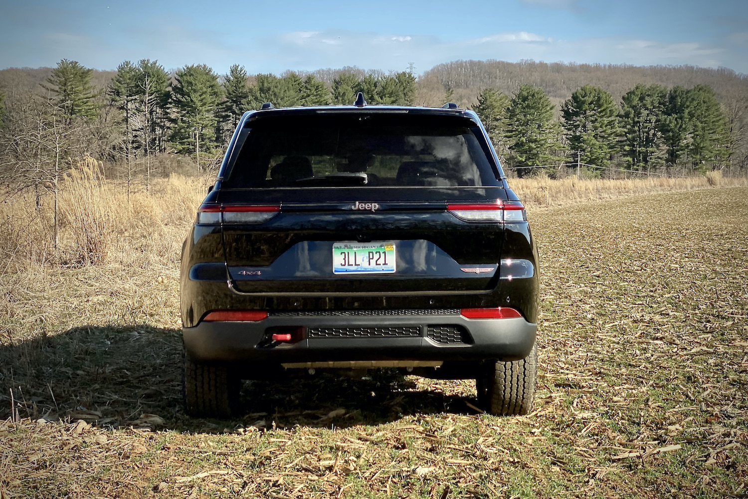 Rear end close up of 2022 Jeep Grand Cherokee Trailhawk in a grassy field with trees in the background.