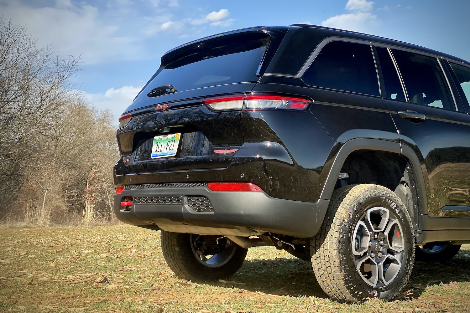 Close up of rear end of 2022 Jeep Grand Cherokee Trailhawk on a grassy field with trees in the background.