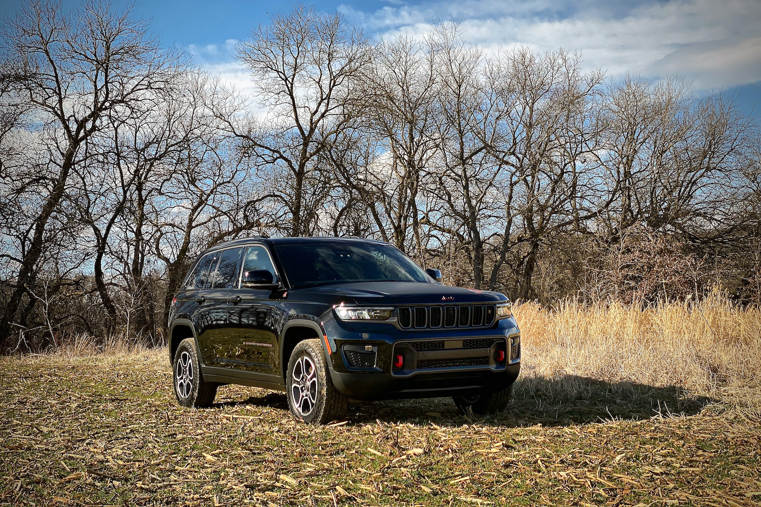 Front view of 2022 Jeep Grand Cherokee Trailhawk from passenger's side in a grassy field with trees in the background.