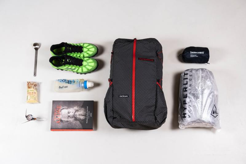 A lightweight backpacking setup including trainers, on a plain background.
