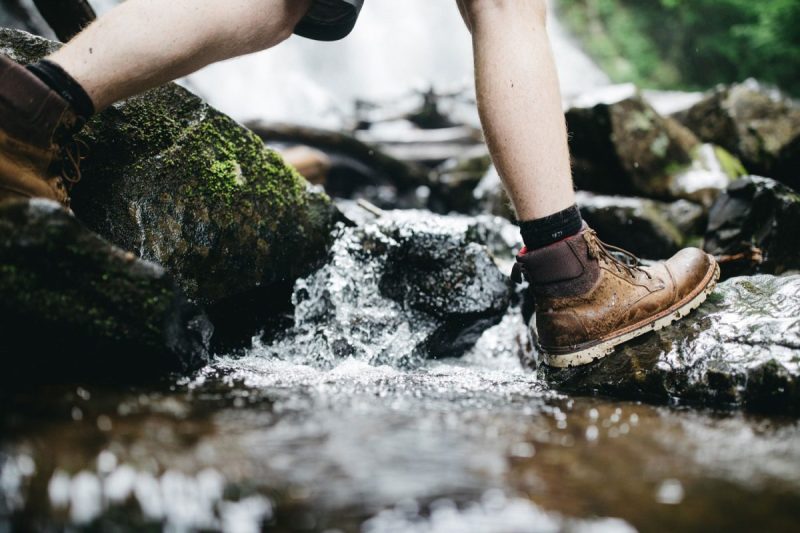 Person in hiking boots crossing stream in the woods.