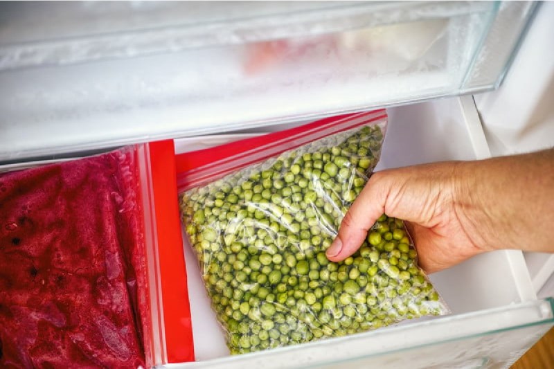 person placing bagged vegetables into the freezer.