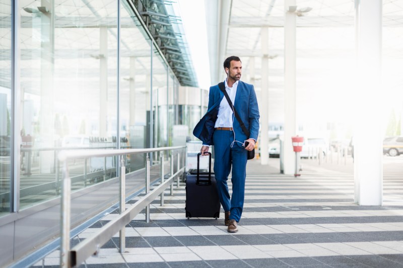 A man in a suit listening to music while hauling his luggage in the airport.