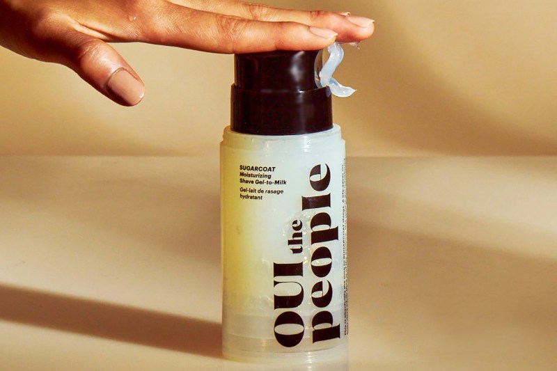 Someone reaches for a tub of Oui the People Sugarcoat Moisturizing Shave Gel-to-Milk.