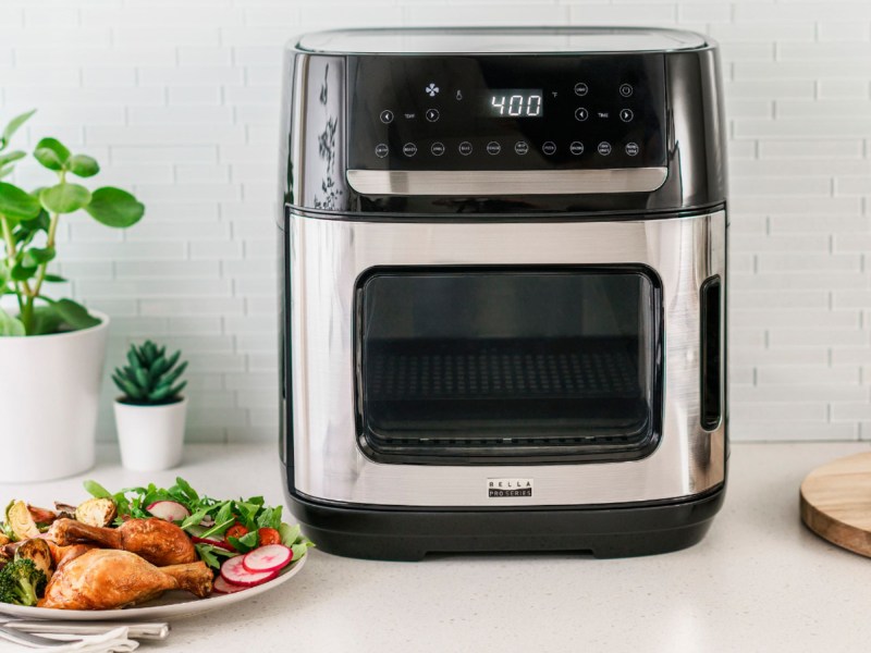 Bella Pro 12.6-quart Pro digital air fryer oven with a prepared meal of chicken drumsticks and salad.