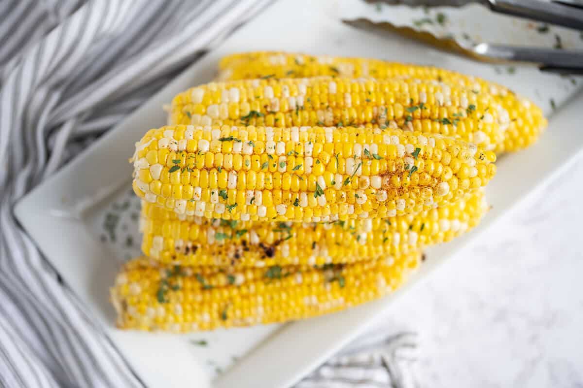 Grilled corn on a tray with herbs.