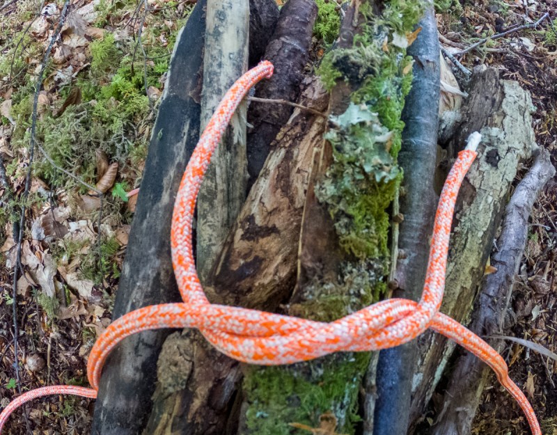 Step 2 of tying a square knot around a bundle of wood