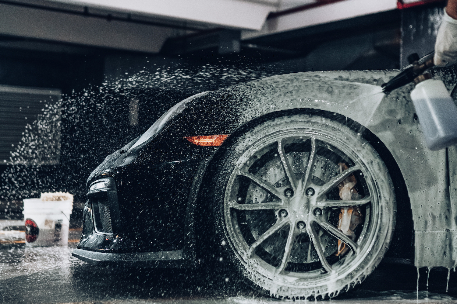Close-up of front end tire of black Porsche 911 being washed with a spray foam gun