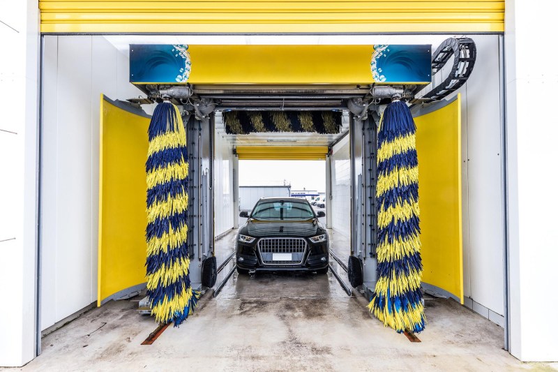 Pequeño lavado internacional de coches con cepillos azules y amarillos con un Audi esperando a ser lavado.