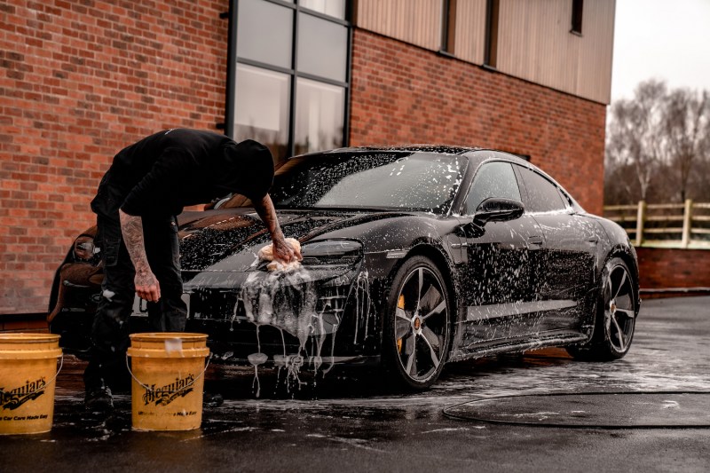 Professional detailer cleaning black Porsche Taycan next to a brick building