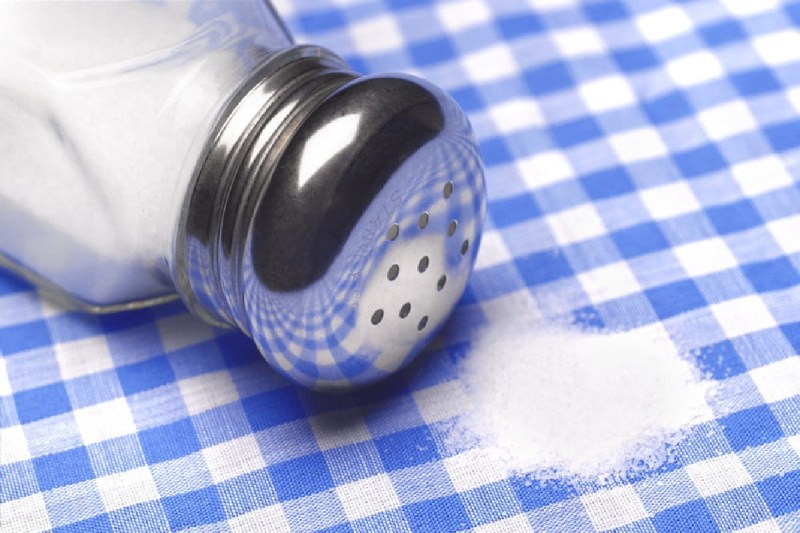 spilled salt next to a clear glass salt shaker.