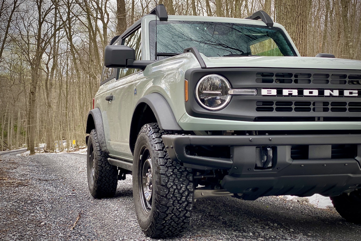 Close up of front end of 2021 Ford Bronco from passenger side on a gravel trail with trees in the back.