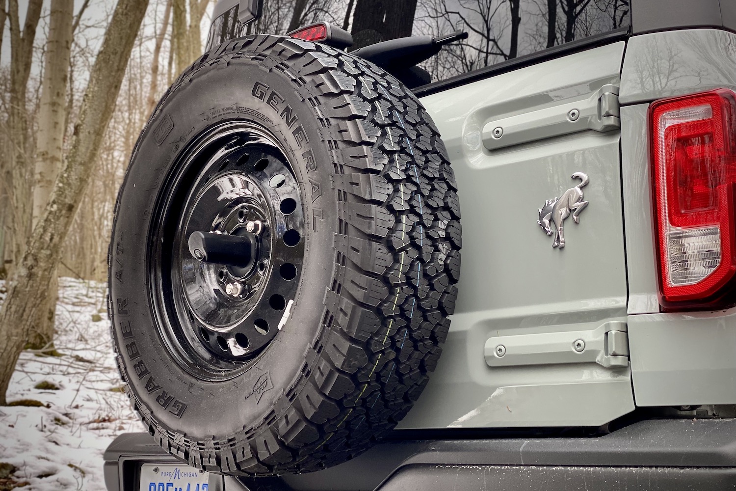 Close up of spare tire on 2021 Ford Bronco and Bronco badge with snow in the back.