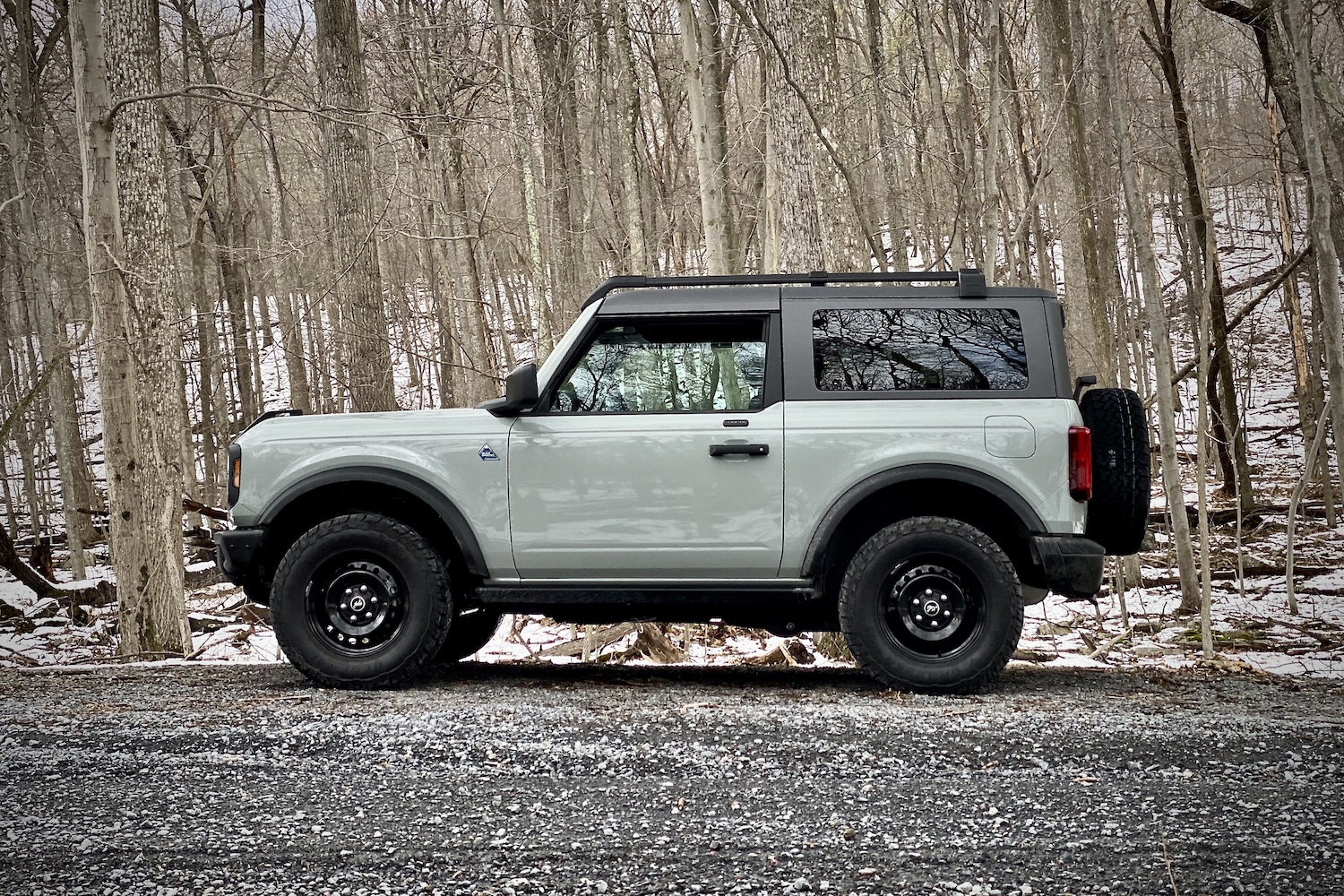 Side view of 2021 Ford Bronco from driver's side on a gravel trail with trees in the back.