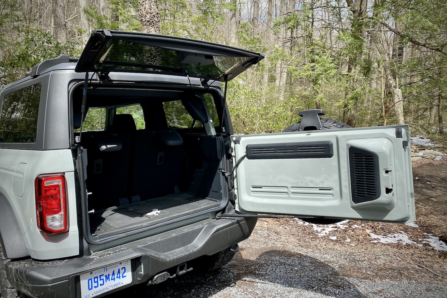 2021 Ford Bronco close up of rear tailgate out and cargo area with rear seats in place with trees in the back.