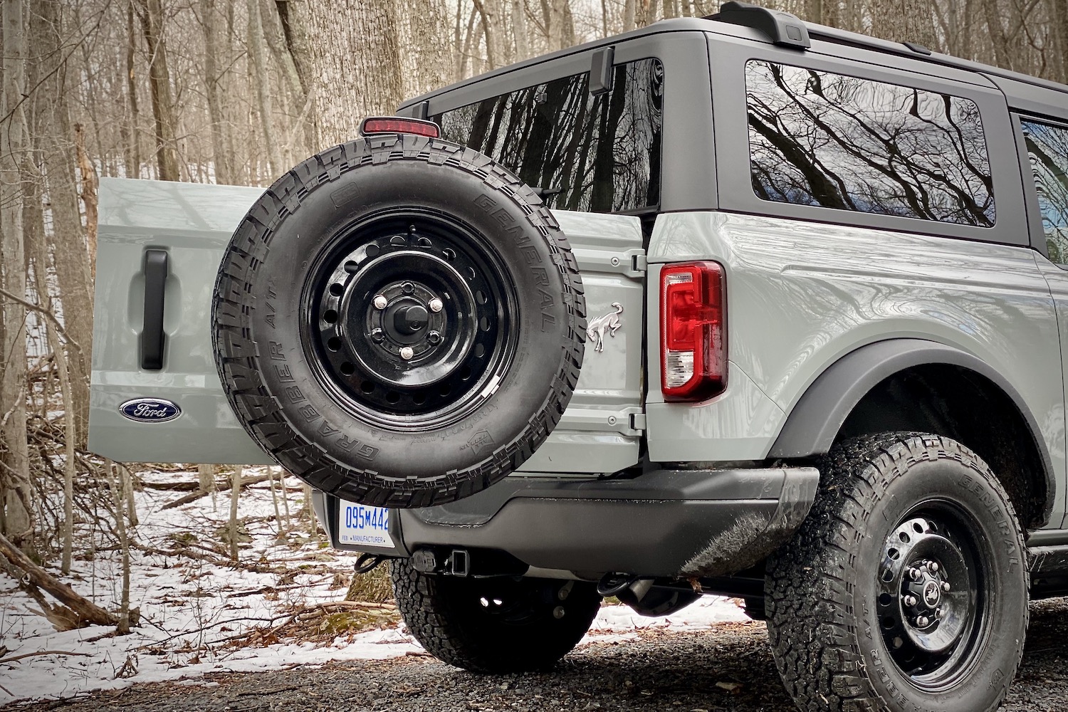 Close up of 2021 Ford Bronco rear tailgate extended out with spare tires with trees in the back.