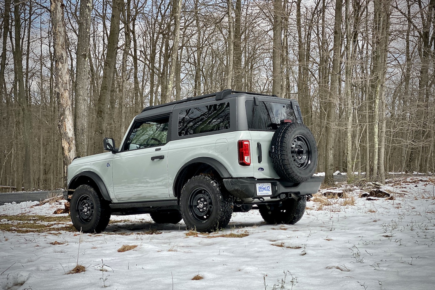 Rear end angle of 2021 Ford Bronco from driver's side in a snowy field with trees in the back.