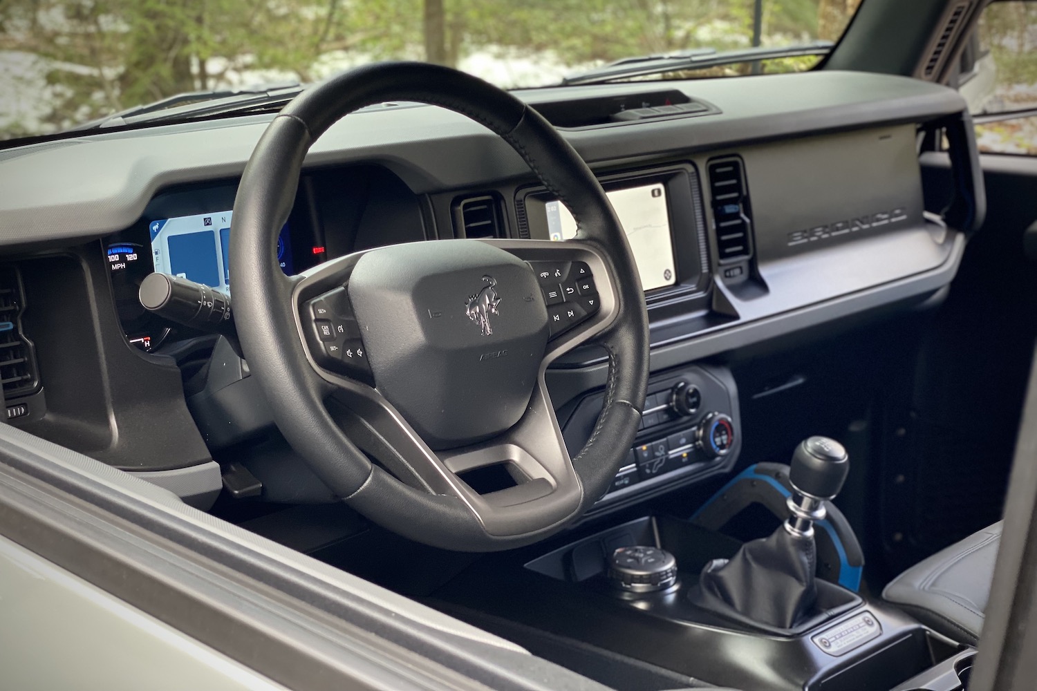 Close up of steering wheel in 2021 Ford Bronco with trees and snow in the back.
