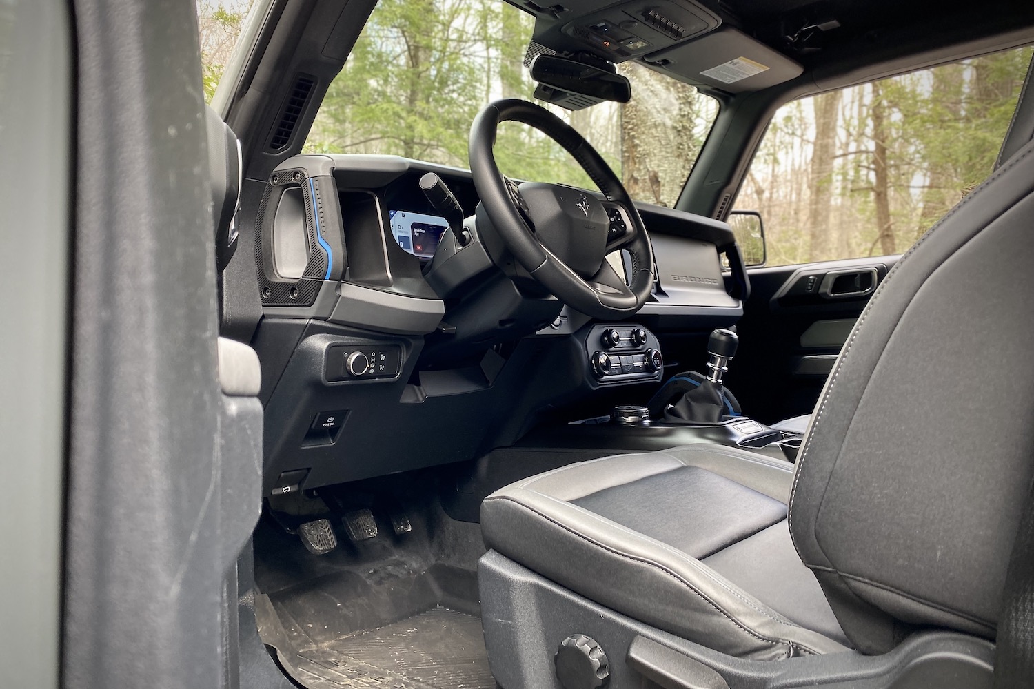 Steering wheel and front driver's seat in 2021 Ford Bronco with trees in the back.