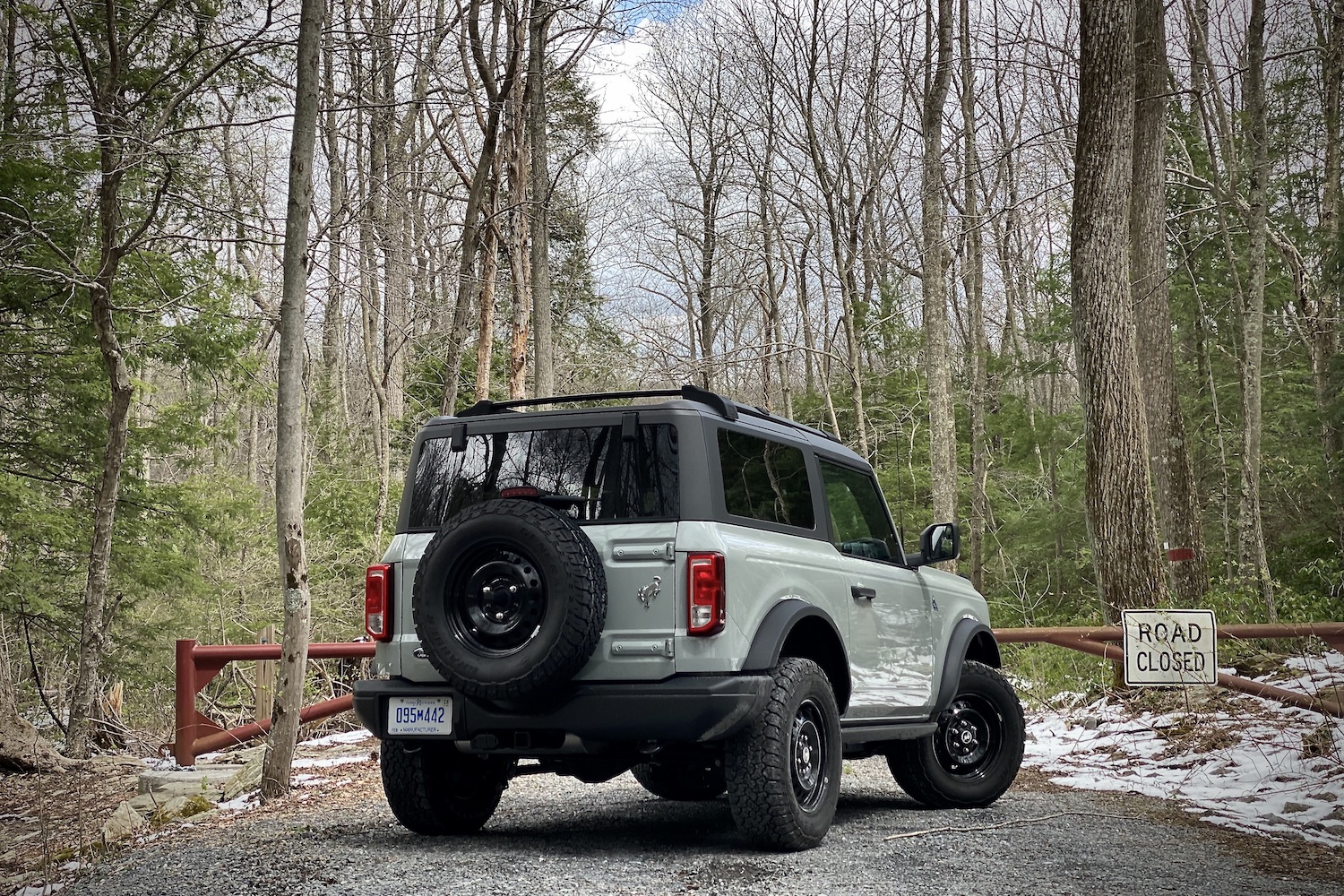 2021 Ford Bronco rear end angle from passenger side in front of a road closed sign on a dirt trail in front of bare trees.