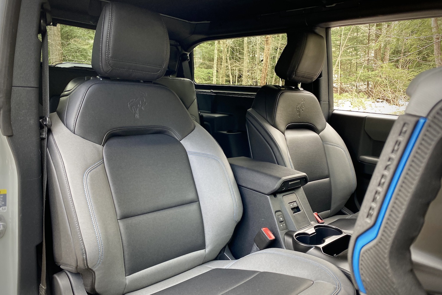 Front seats in the 2021 Ford Bronco from the passenger side from outside the SUV with trees in the back.