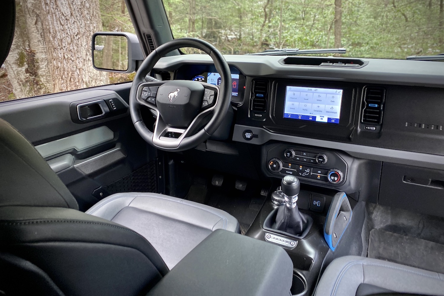 Steering wheel and dashboard in the 2021 Ford Bronco from the back seats with trees in the back.