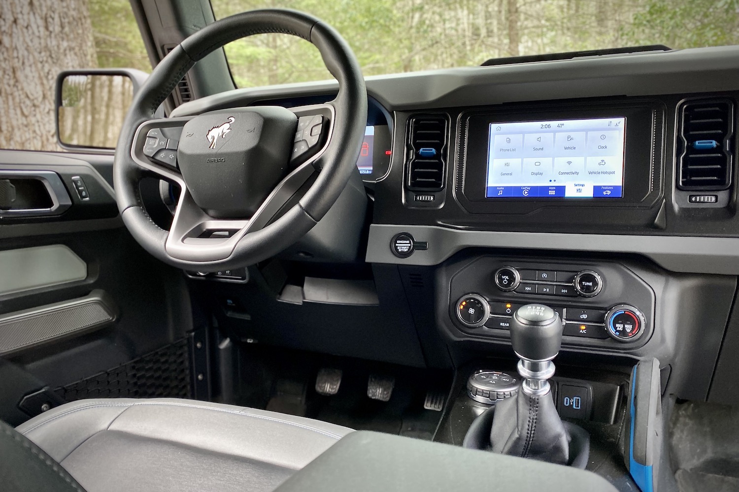 Close up of steering wheel and infotainment system in 2021 Ford Bronco with trees in the back.