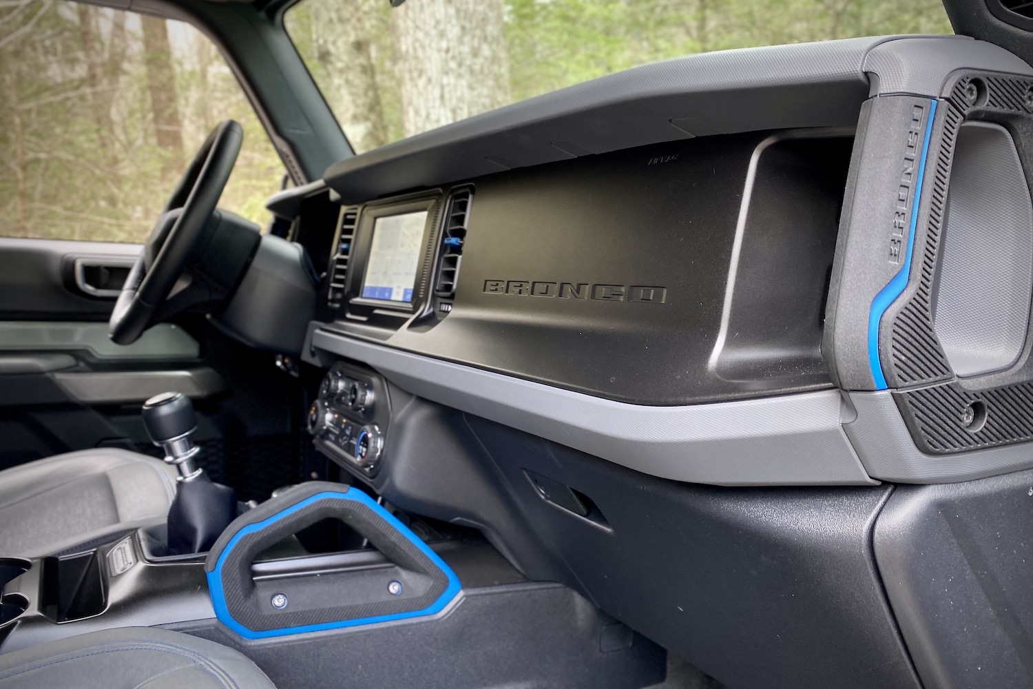 Close up of 2021 Ford Bronco dashboard from passenger side from outside the SUV with trees in the back.