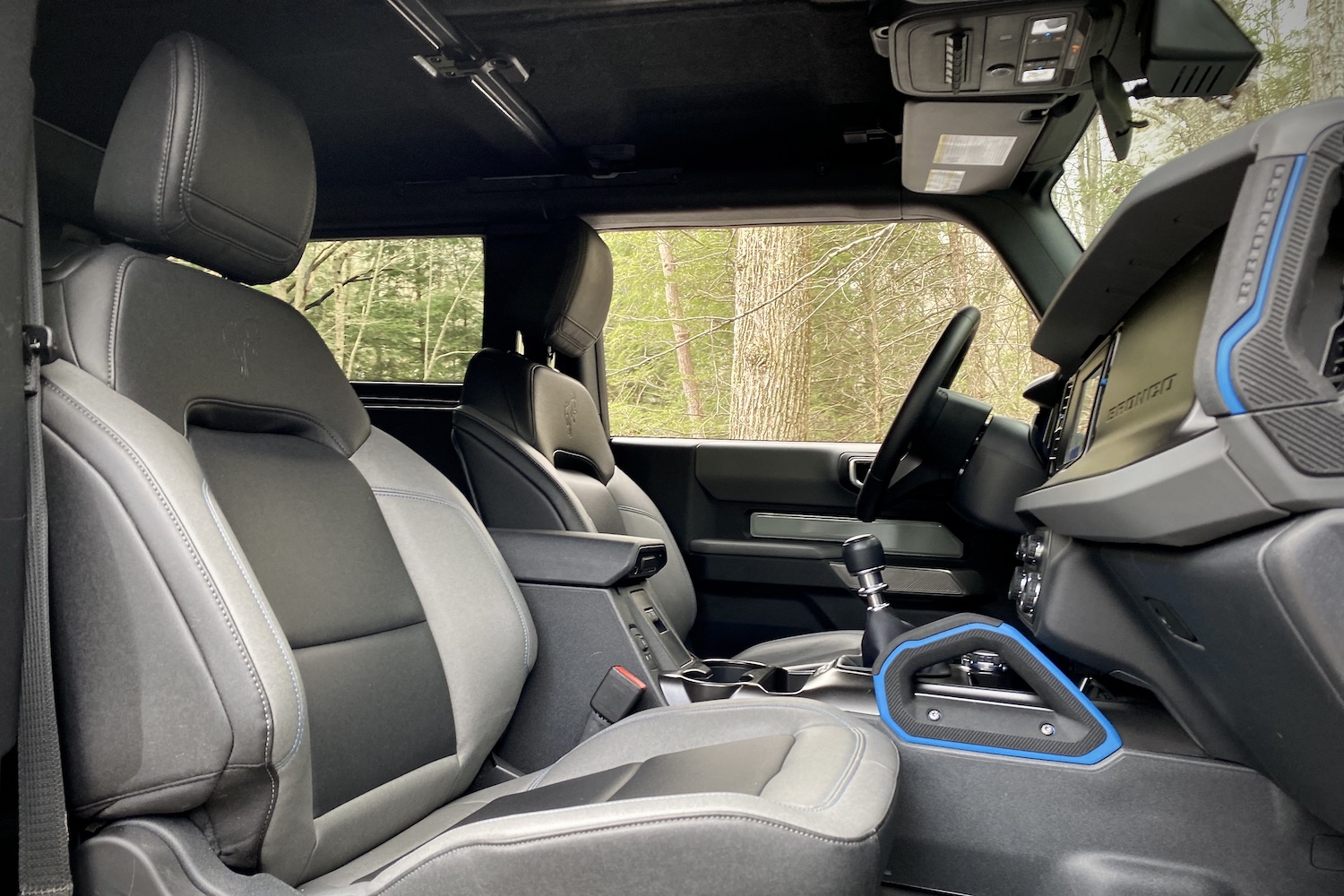 Front seats in the 2021 Ford Bronco from passenger side with trees in the back.