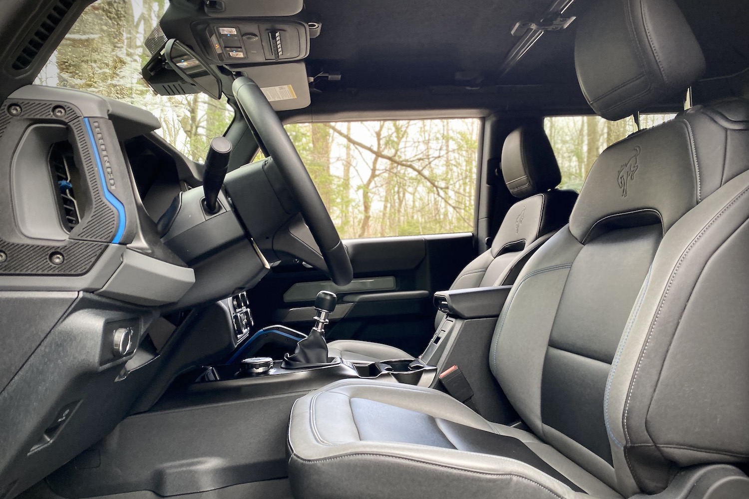 Side view of front seats in 2021 Ford Bronco from driver's side with trees in the back.