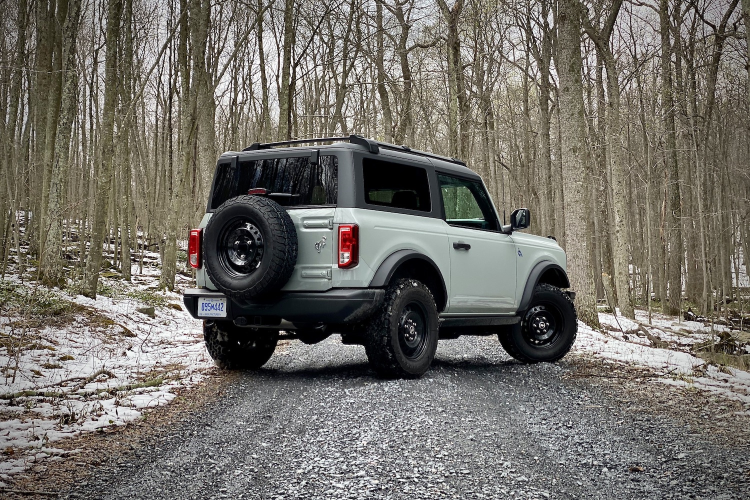 2021 Ford Bronco rear end angle from passenger side on a gravel trail in front of bare trees with snow on the ground.