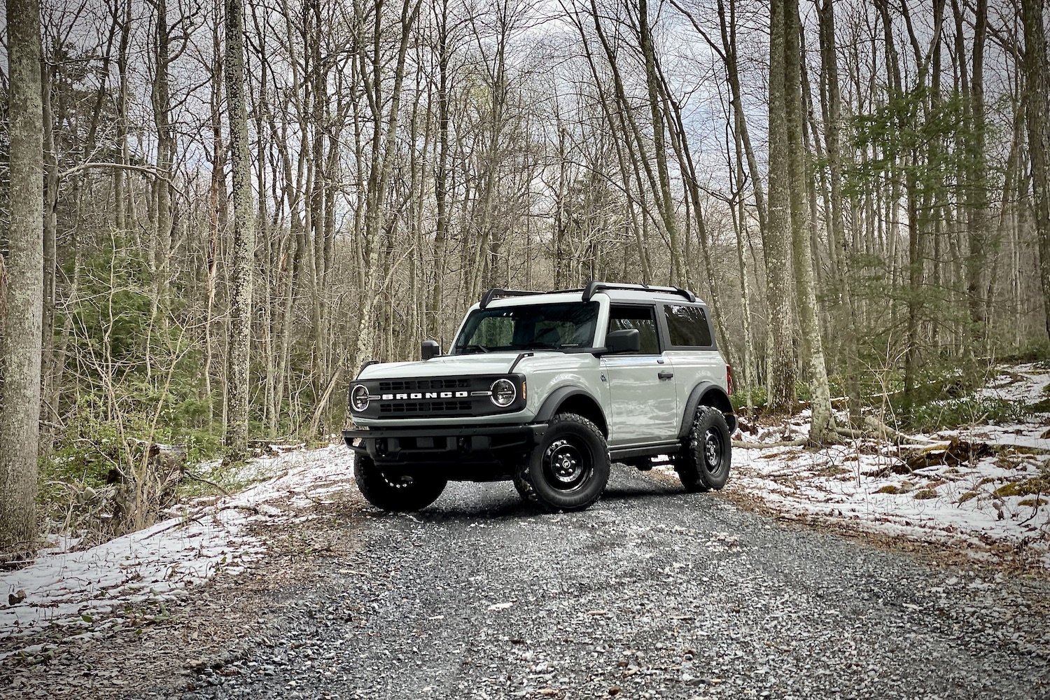 2021 Ford Bronco front end angle from driver's side on a gravel trail in front of bare trees with snow on the ground.