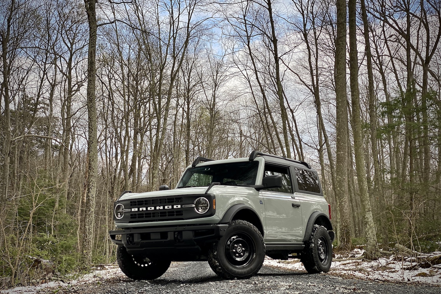 2021 Ford Bronco front end angle from below driver's side with trees in the back on a gravel trail.