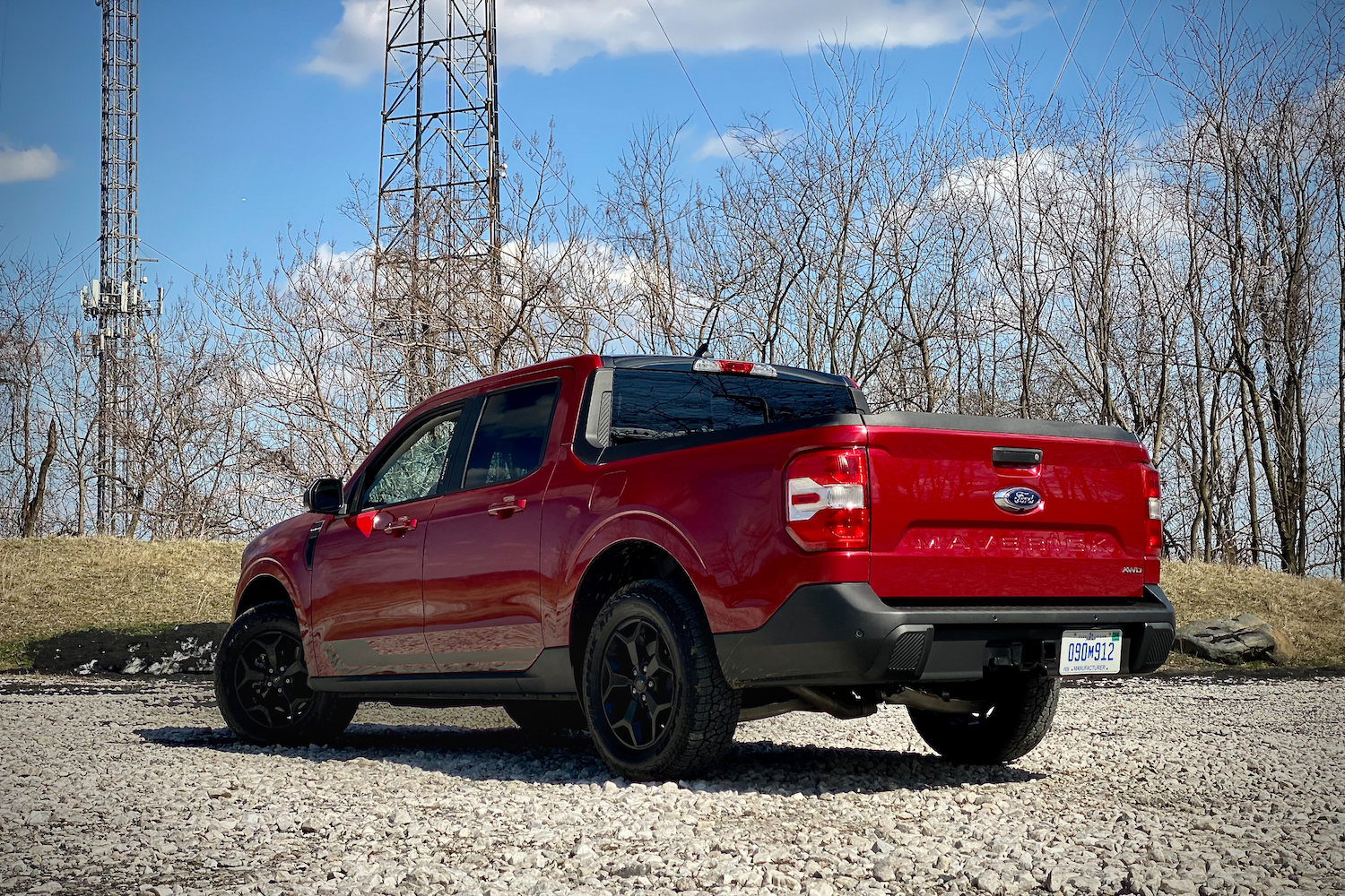 Rear end angle of 2022 Ford Maverick from driver's side on a gravel parking with blue skies.